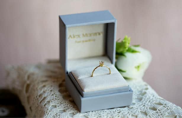 A lilac Alex Monroe hinged jewellery ring box containing a diamond engagement ring.