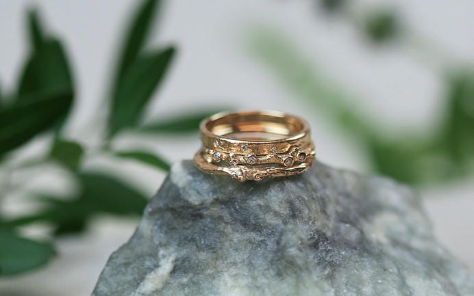 Stack of three 18ct rose gold rings on a light grey stone with foliage behind..