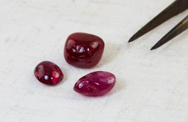 Three deep red ruby gemstones scattered on a white surface.