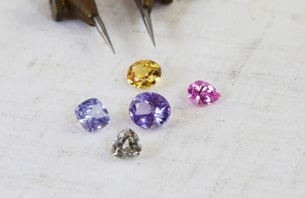 Five coloured sapphire gemstones scattered on a white surface.