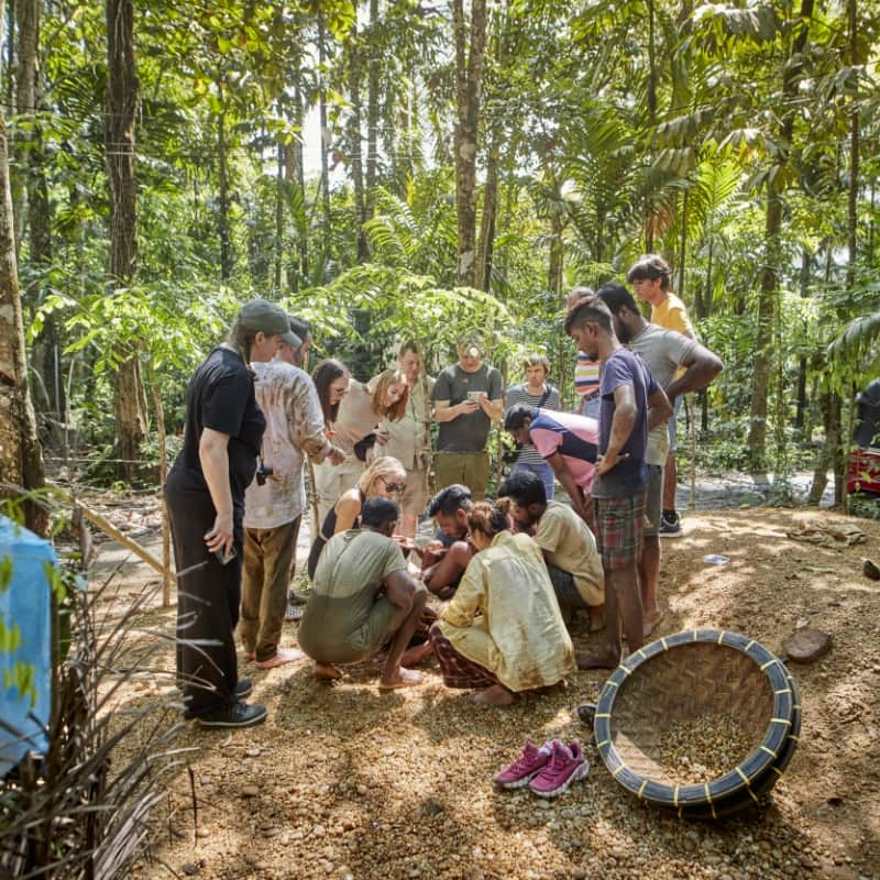 A group of people in the middle of a rainforest clearing, gathered around a mining area on the ground.