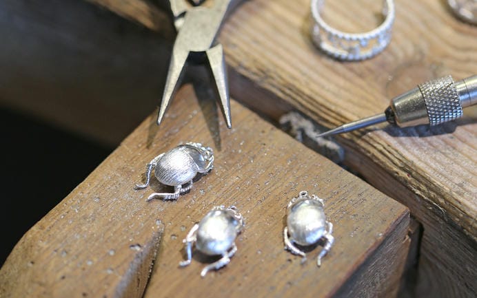 Three silver beetle castings on a jewellers bench peg ready to be finished and put on a necklace chain.