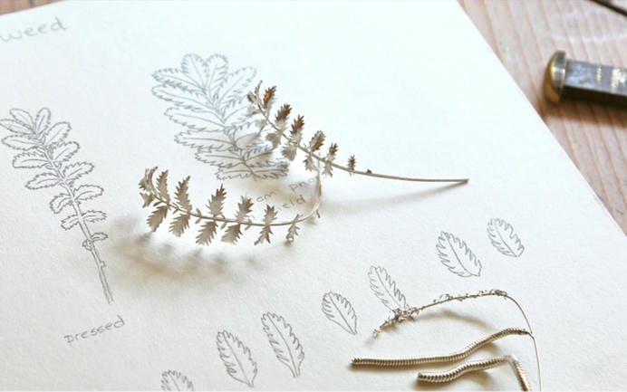 A pair of leafy branches made from silver resting atop a sketchbook with corresponding leaf sketches.