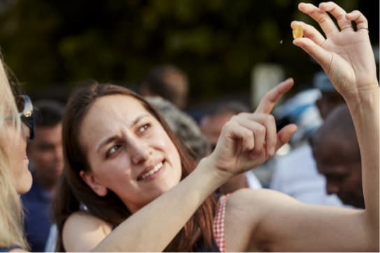 Susie holds a rough, uncut yellow sapphire up to the sun to inspect it at a gemstone street market in Sri Lanka.