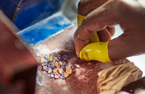A worker with yellow fingertip gloves on, sorting through raw uncut coloured sapphires.