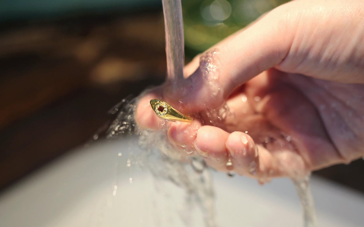 Rinsing a gold ring under a running tap.