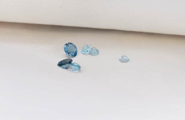 Six pale blue topaz gemstones scattered on a white surface.