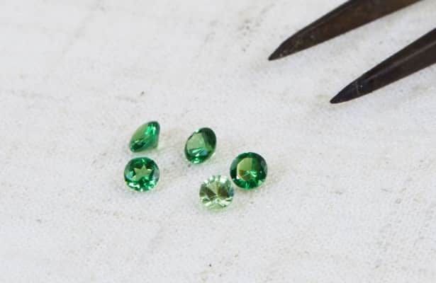 Five green tsavorite gemstones scattered on a white surface.