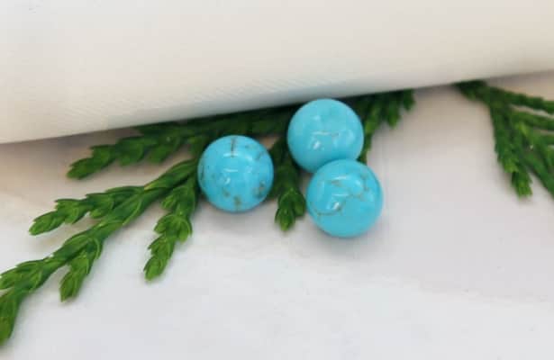 The round bright blue green turquoise gemstones scattered on a white surface.