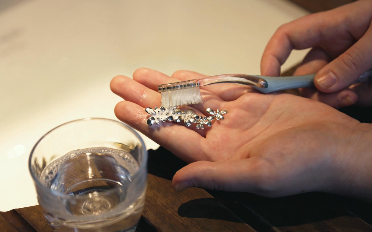 Cleaning a piece of silver jewellery using a toothbrush and a glass or soapy water.
