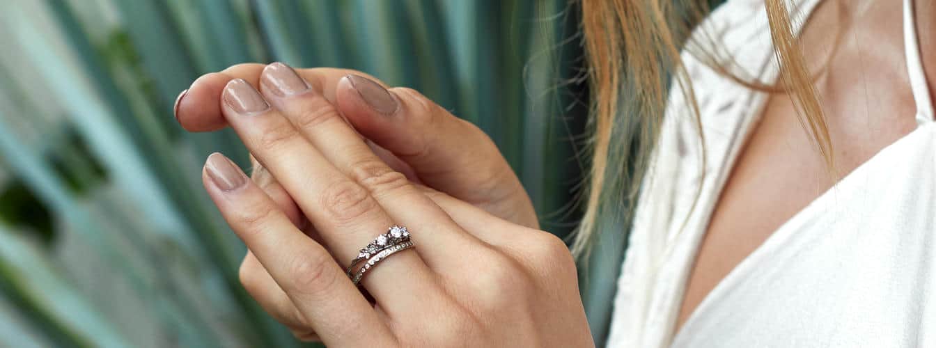 Woman wearing a white gold wedding band set with diamonds and a diamond trilogy white gold engagement ring.