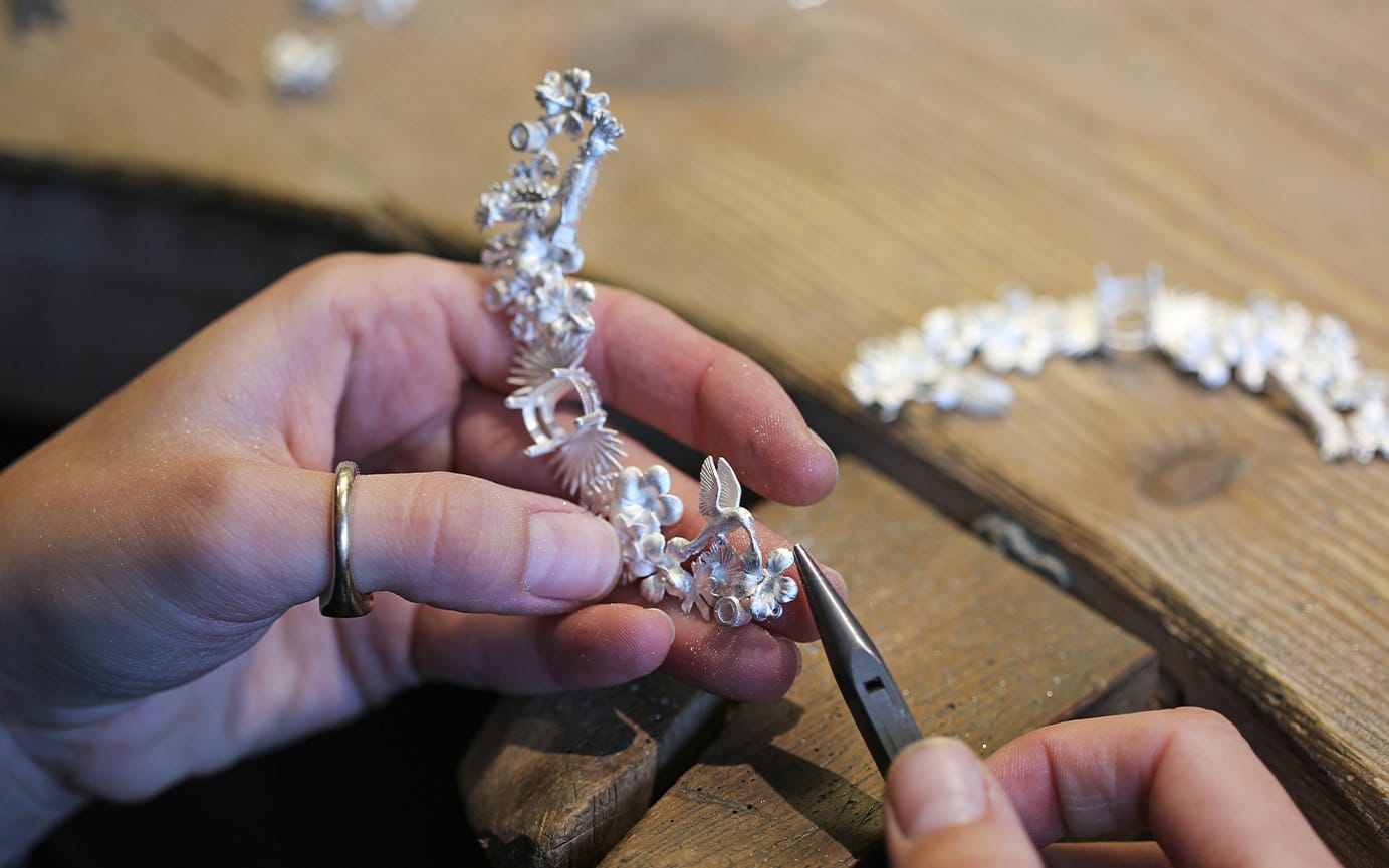 Jeweller at their jewellers bench working on a large silver piece of jewellery.